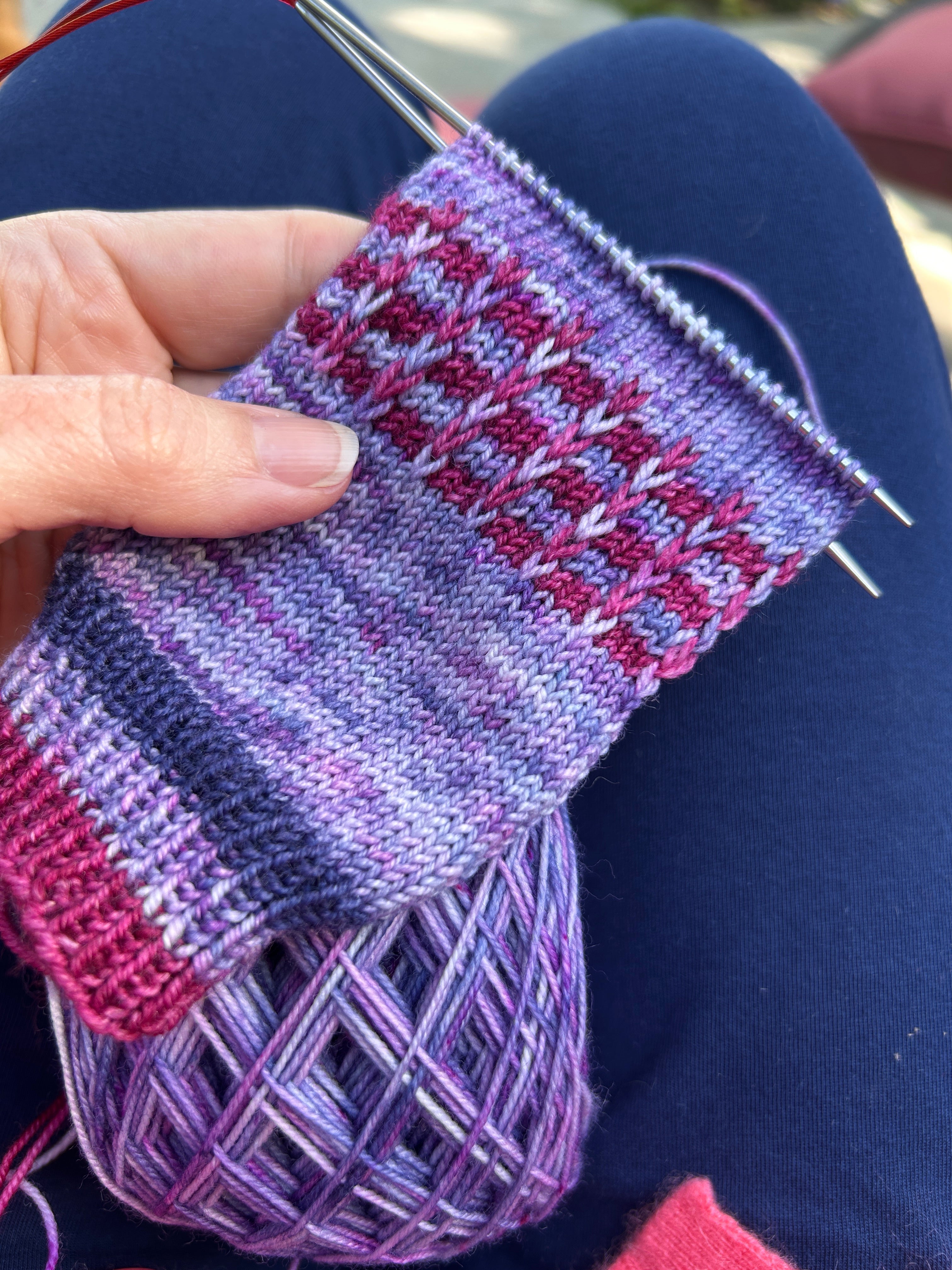 a hand knit sock in progress in the colors purple, blue, and magenta