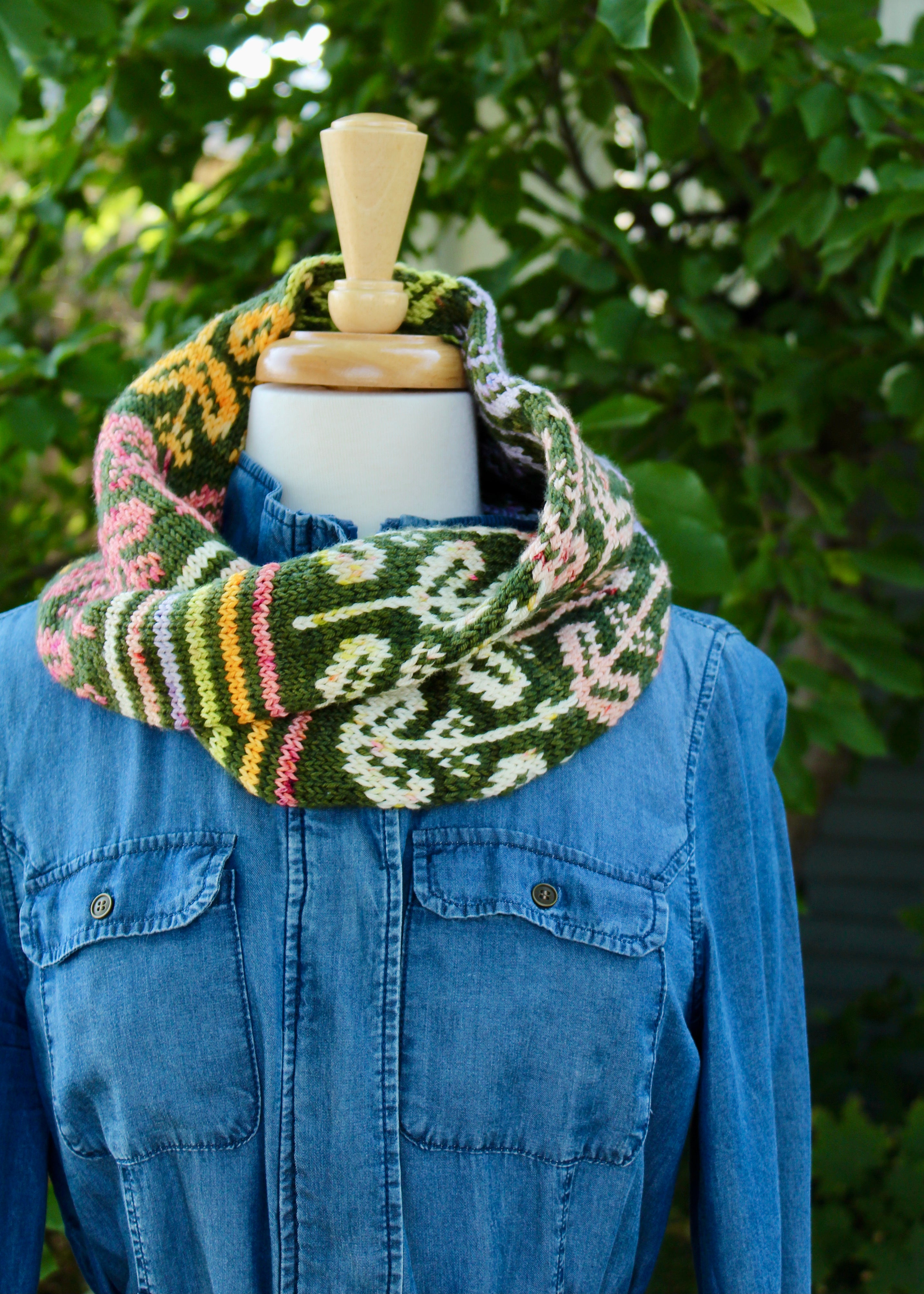 A bright green and cheerful floral print cowl hangs on a mannequin wearing a denim shirt. The cowl is called Scandi Bloom and is ispired by Scandinavian style print patterns.