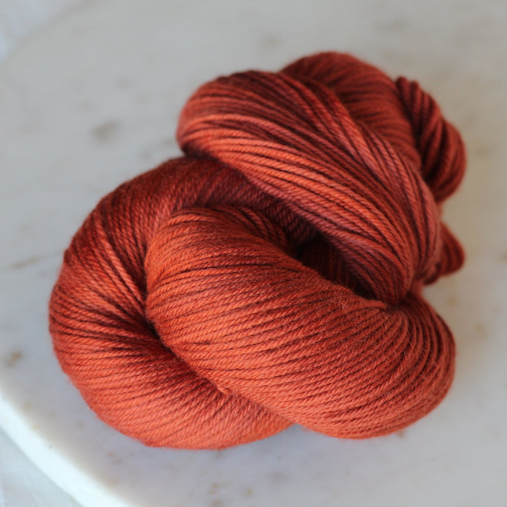 Ball of rust orange yarn on a white plate with a white background