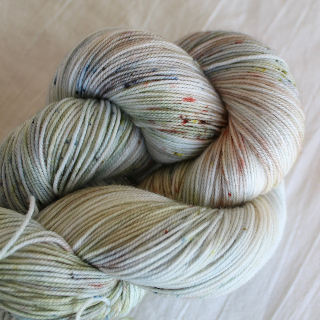 Bundles of hand-dyed yarn in pale blue and green shades, displayed on a wooden surface, with a plant in the background.
