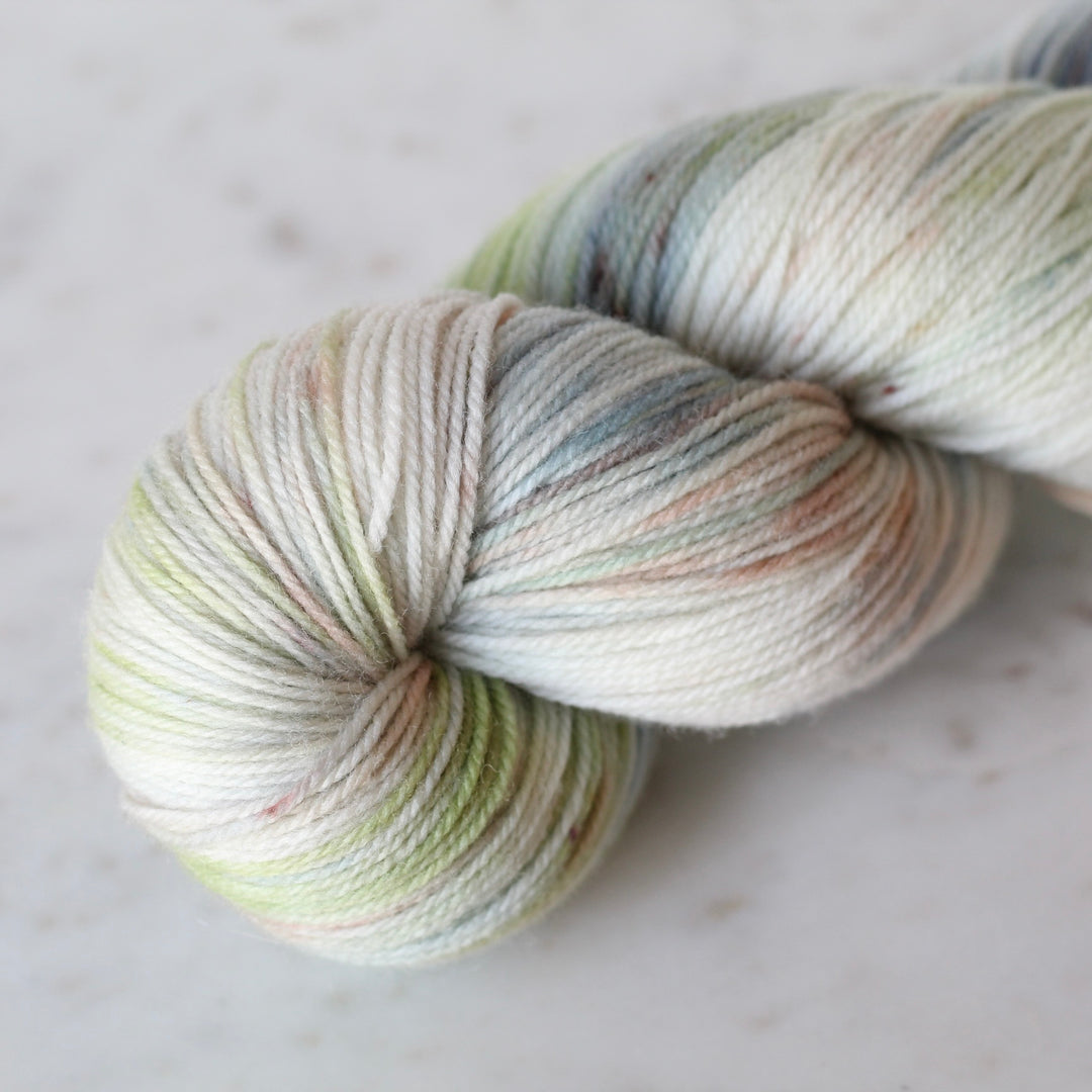 Skein of Cream yarn with blue and soft green washes on a light surface