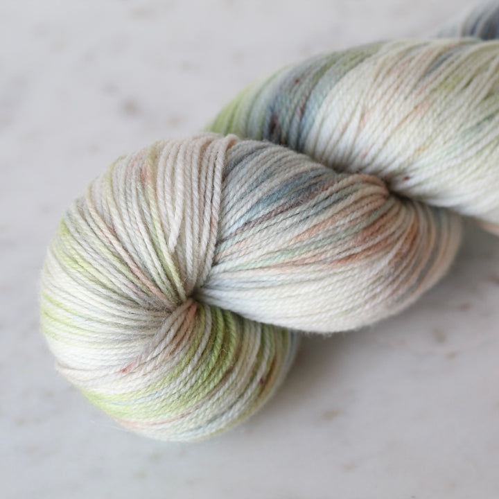 Skein of Cream yarn with blue and soft green washes on a light surface