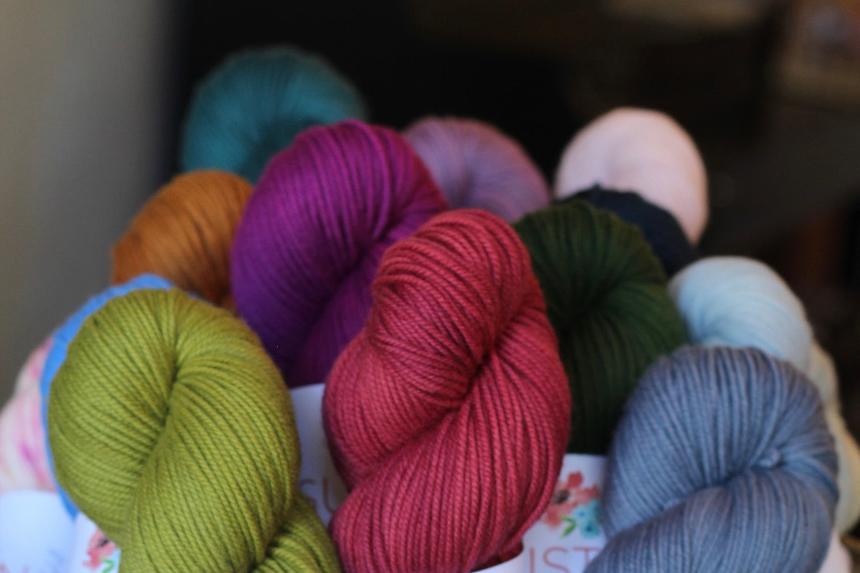 Assorted skeins of yarn in various colors in a basket with visible labels.