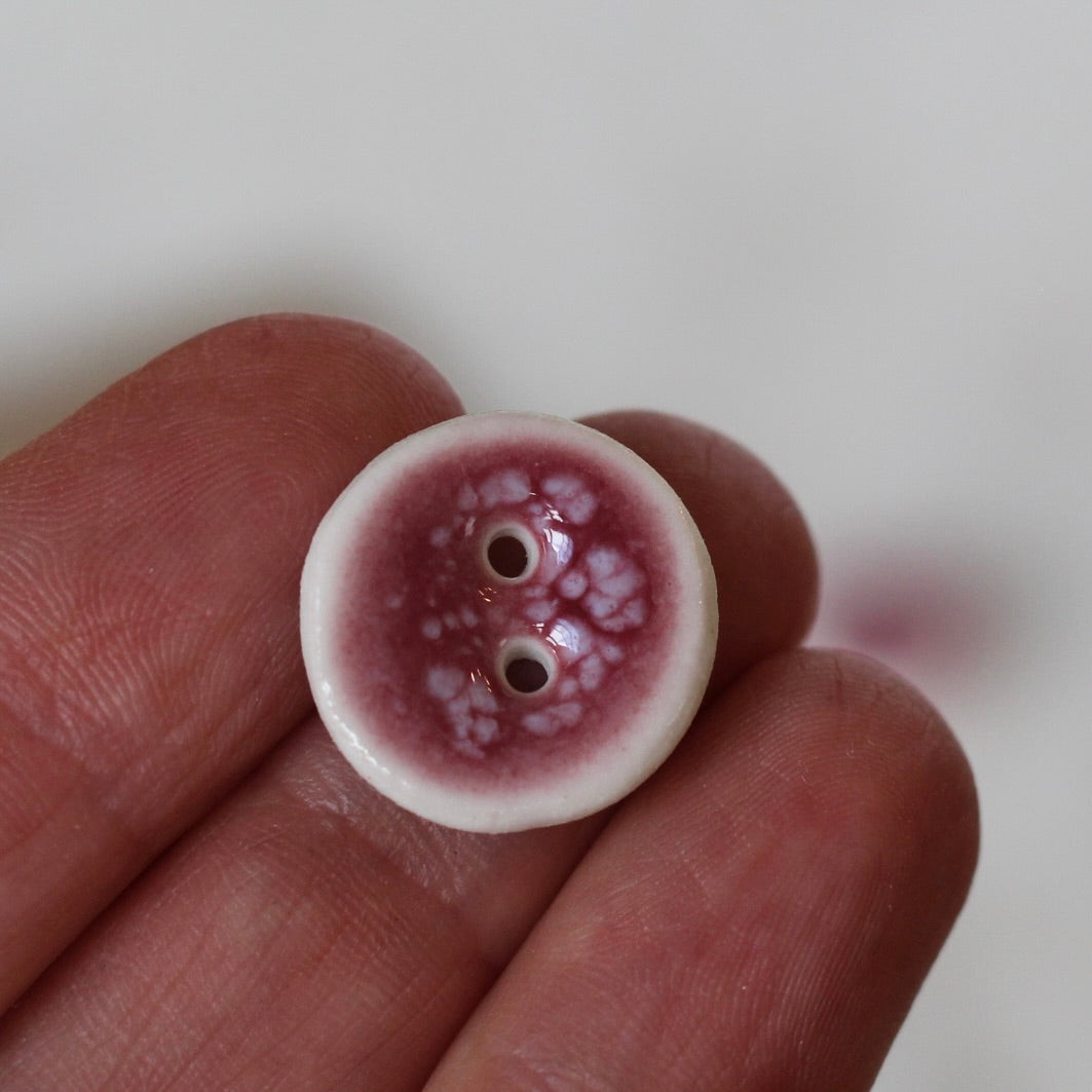 Small ceramic button with a marbled design held between fingers on a white background
