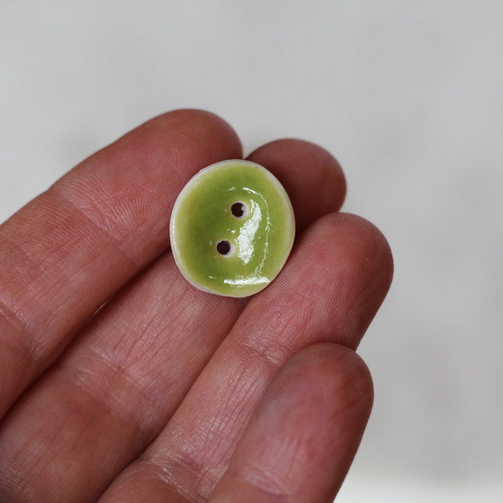 Green button held between fingers against a white background