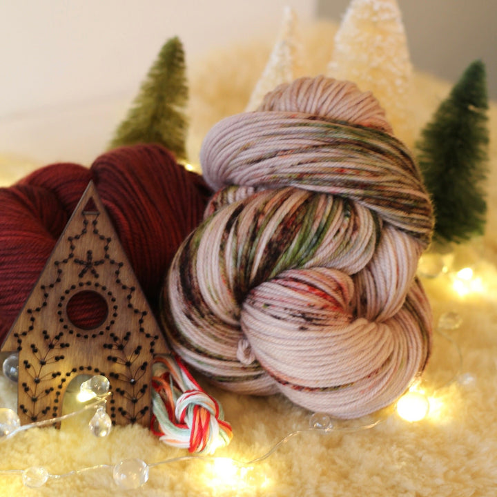 Two skeins of yarn in red, multicolored, and white on a decorative surface with Christmas trees and lights.