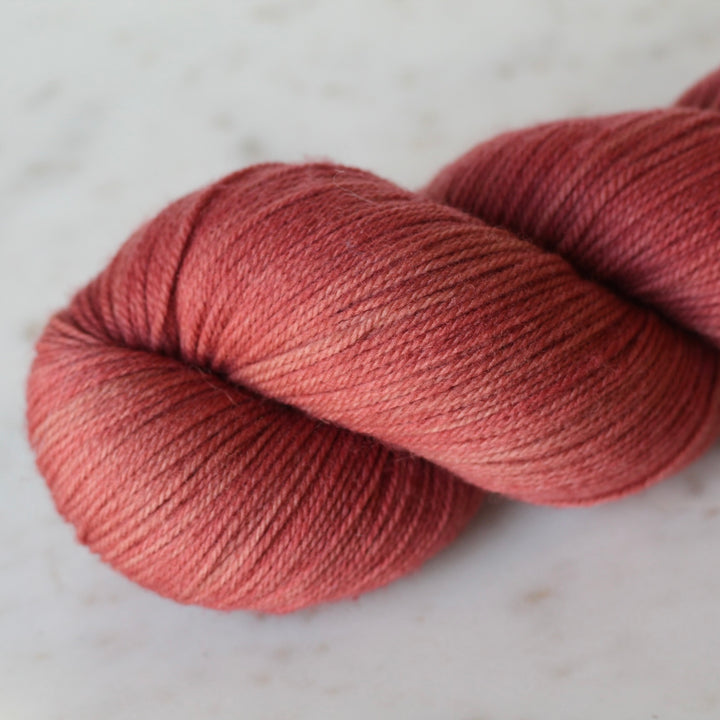 Ball of Deep Coral  yarn on a light marble background