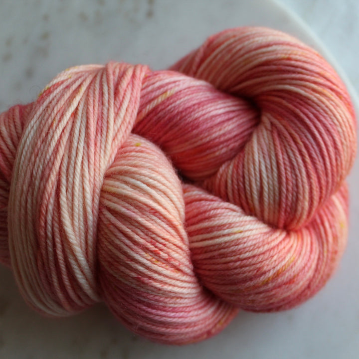 A skein of hand-dyed yarn in pink and white variegated color.