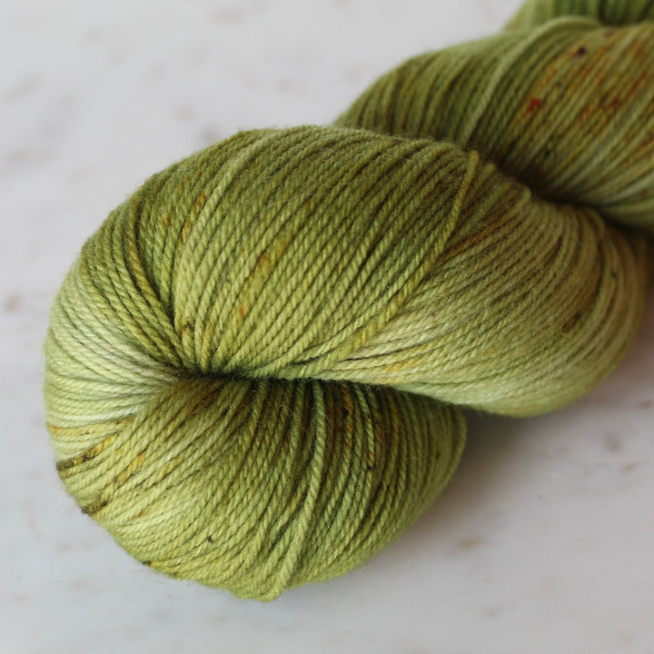 One skein of mossy green yarn on a light beige surface
